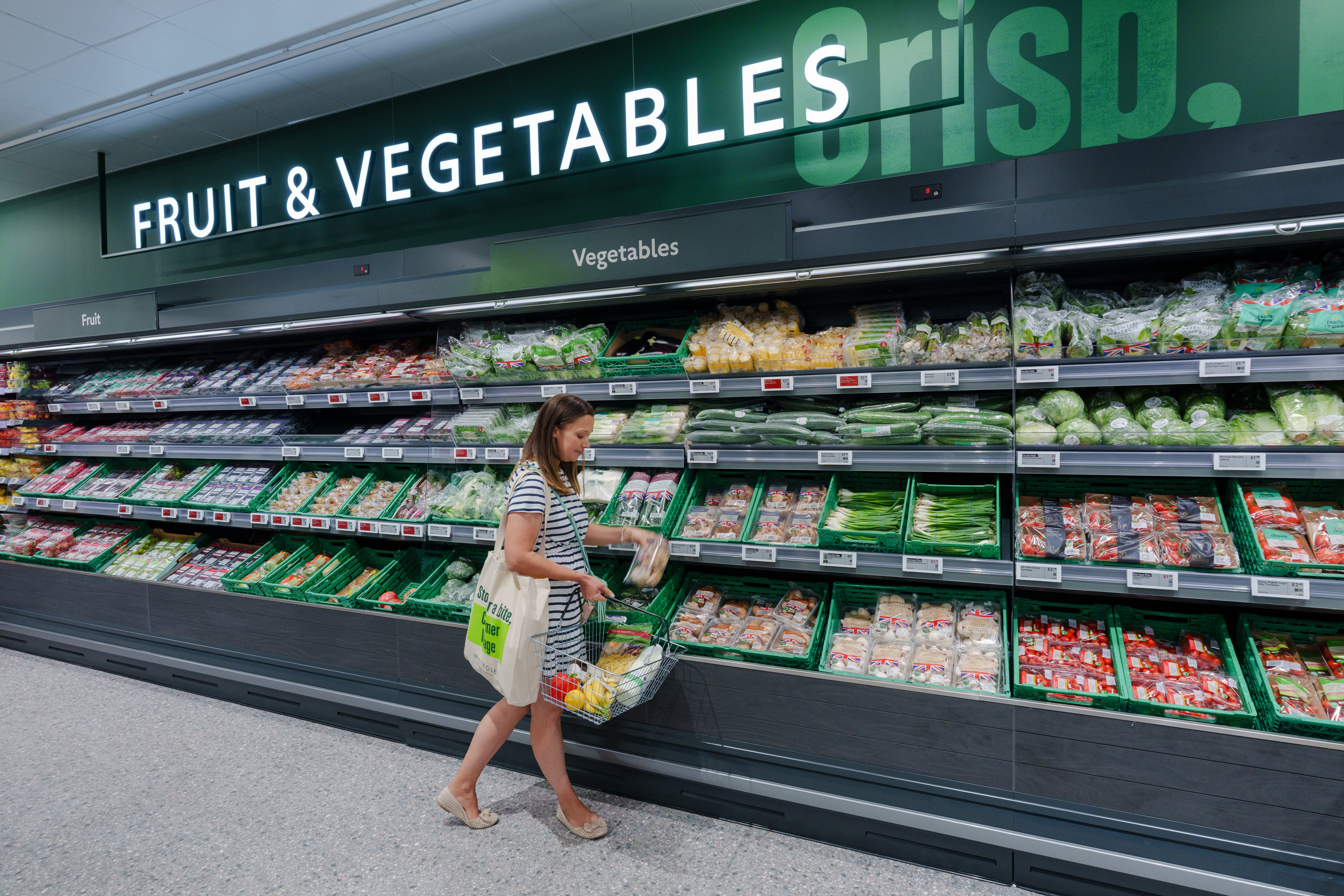 Woman with shopping basket walking in Waitrose Fruit and Vegetables section