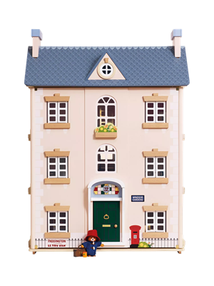Three-story wooden dollhouse painted light pink with white quoins, a blue roof, and green front door. Features a Paddington Bear figure at the entrance, a red postbox, and a sign reading Windsor Gardens.