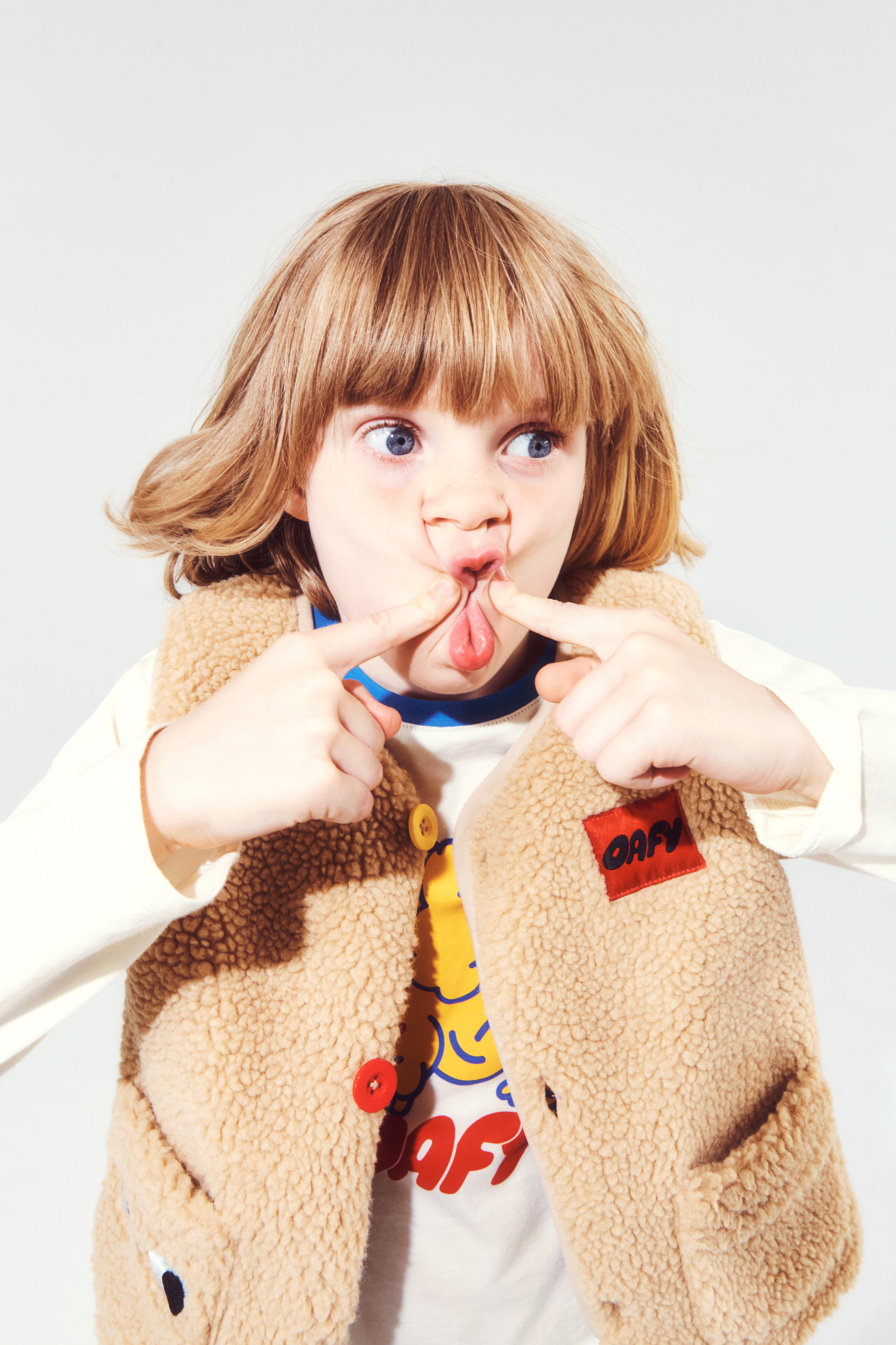 A child making a funny face by pinching their lips together with two fingers, wearing a fleece vest with an 
